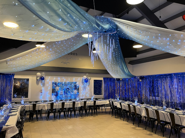 Salle de réception décorée de voilages bleus et de guirlandes lumineuses aux Murmures du Lignon.