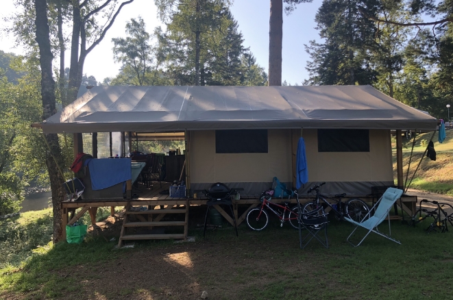 Grande tente lodge sur pilotis avec terrasse couverte et vélos dans un cadre naturel en Haute-Loire.