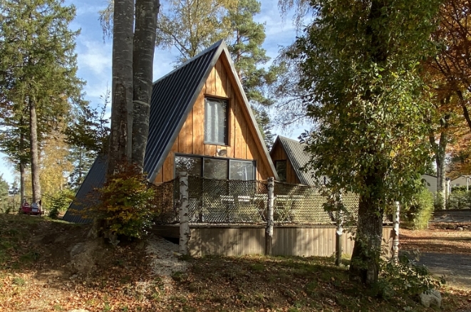 Cabane en bois au toit triangulaire avec terrasse, nichée dans la forêt aux Murmures du Lignon.