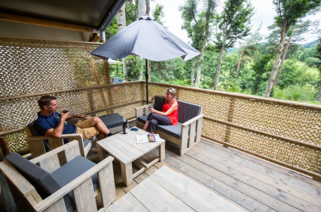 Couple installé sur la terrasse d'un hébergement avec salon de jardin et parasol en Haute-Loire.