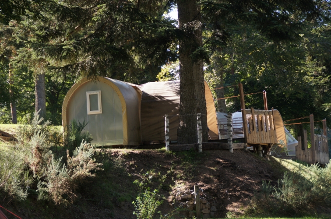 Hébergement insolite de forme arrondie avec terrasse, installé dans un environnement forestier.